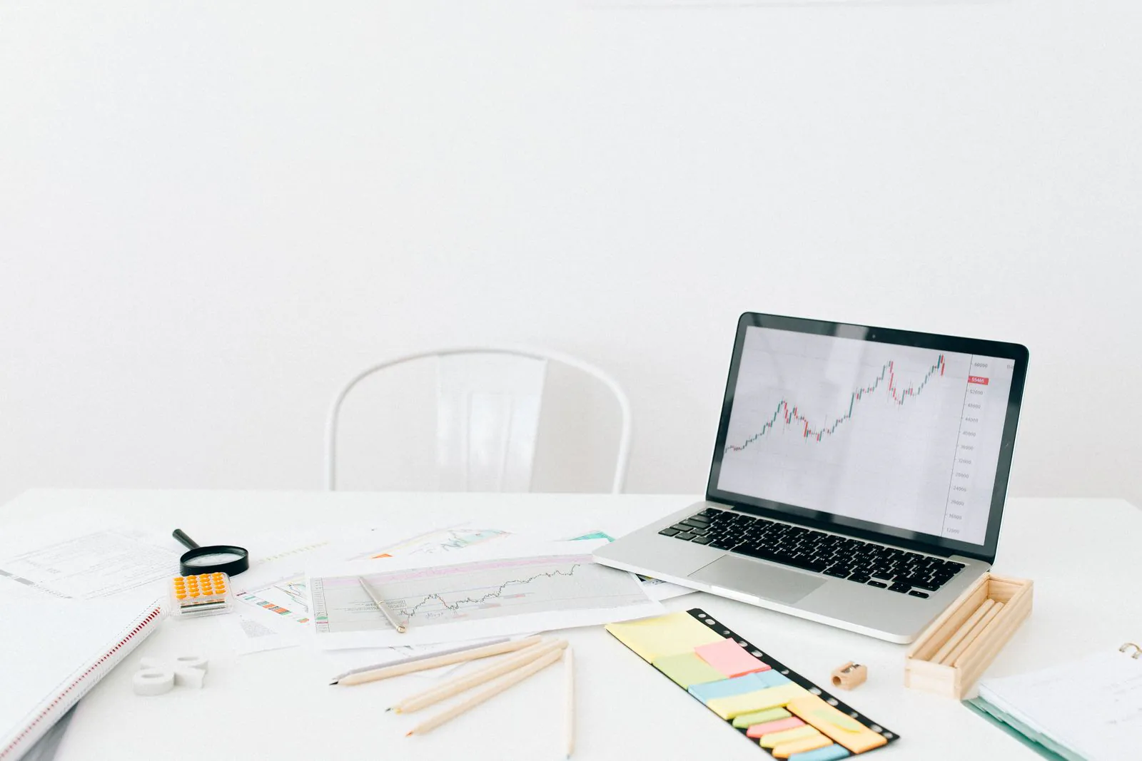 Laptop showing a price chart beside notes and printed figures on a desk