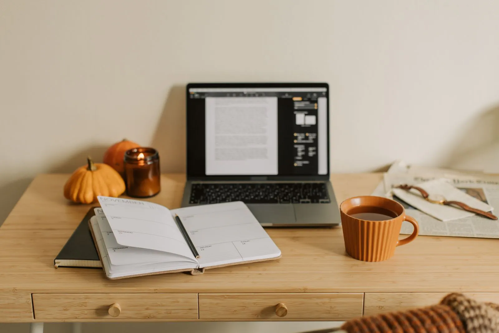 Laptop and notebook with financial records on a desk beside a cup of tea