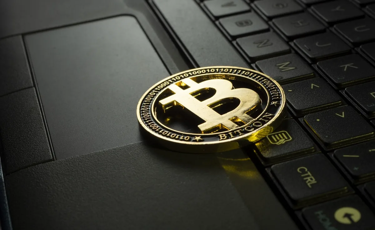 A gold Bitcoin coin resting on a laptop keyboard, representing crypto-native payouts