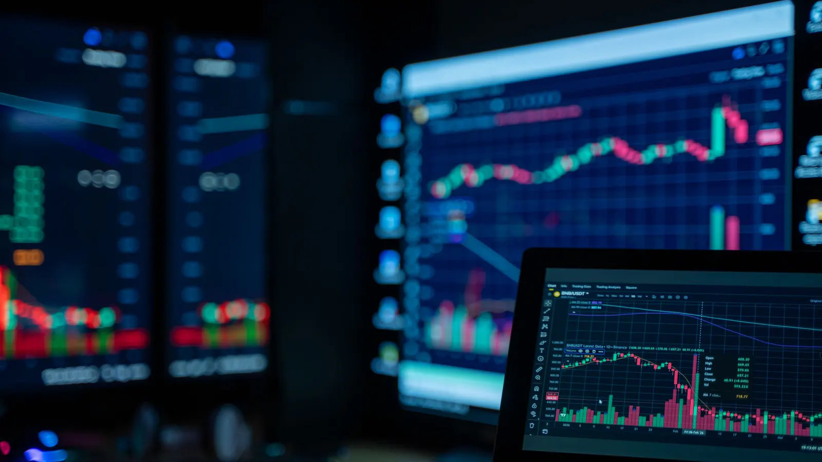 Trading screens showing candlestick charts on several monitors