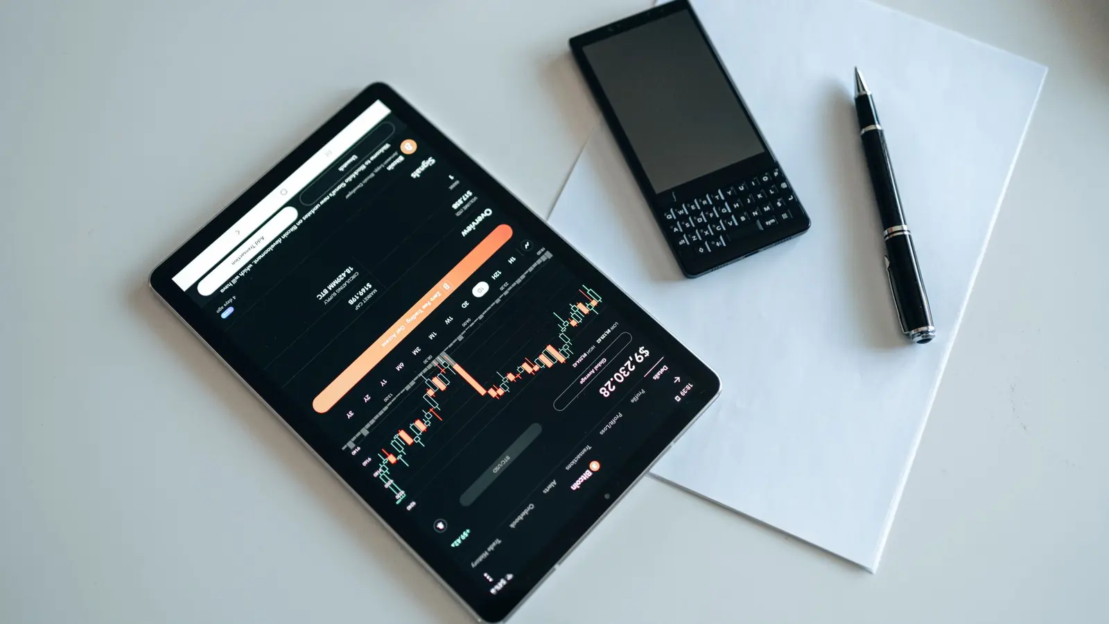 A tablet showing a price chart next to a phone and pen