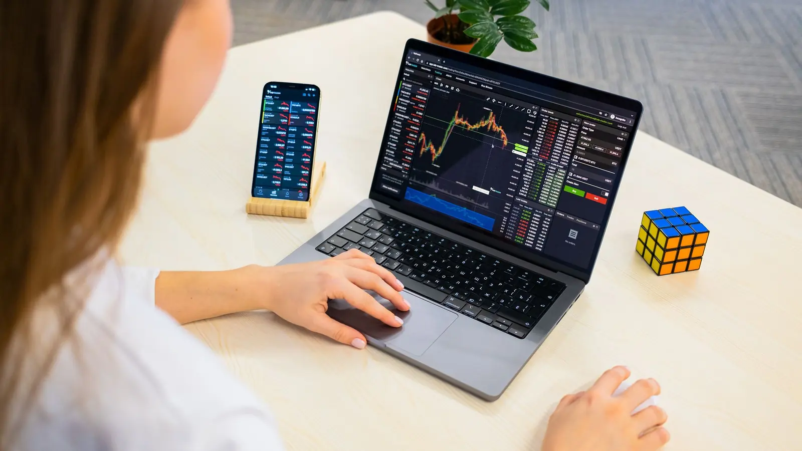 A trader studying a candlestick chart on a laptop next to a phone