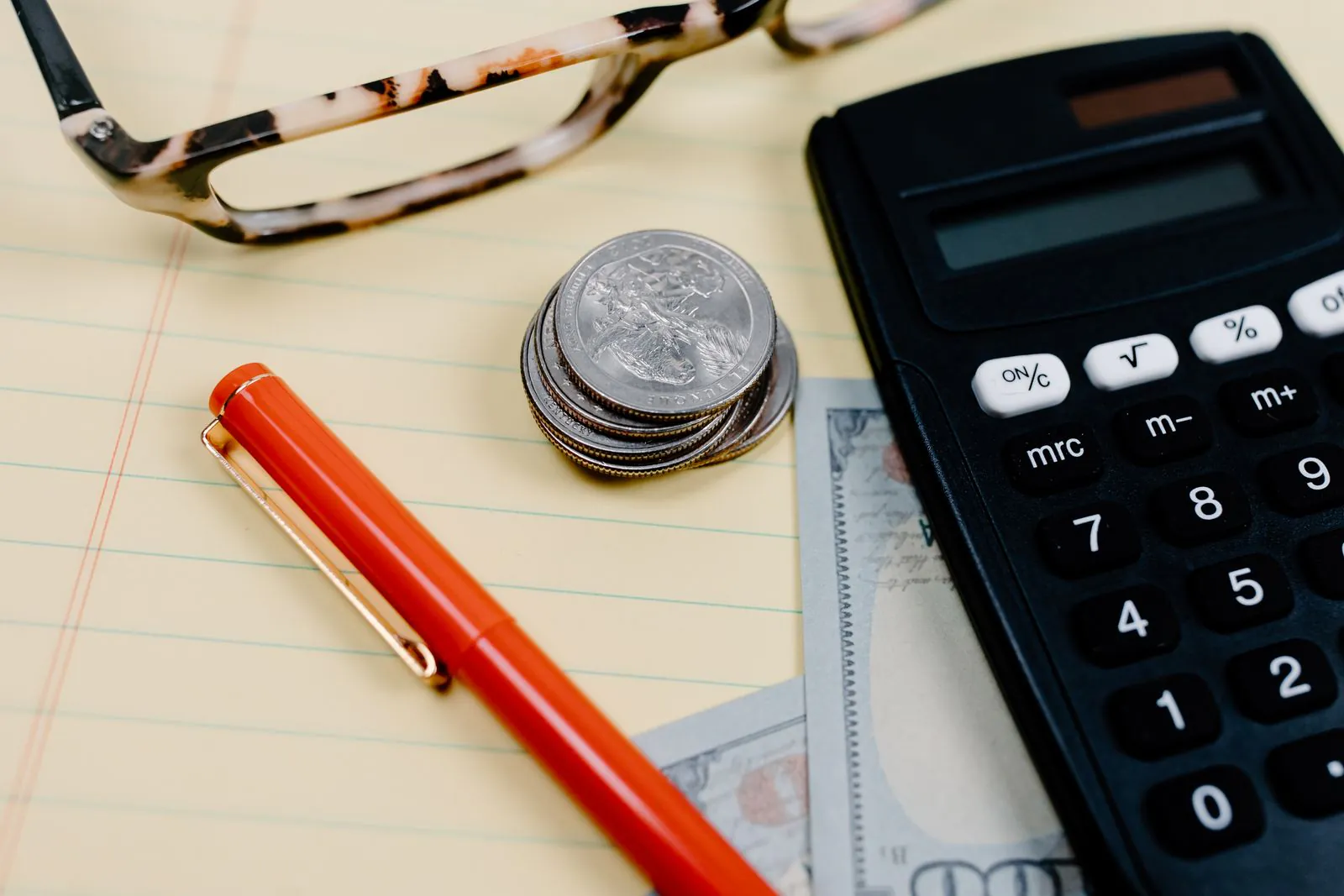 Calculator, coins, banknotes and a pen on a notepad, working out the cost of a prop firm challenge