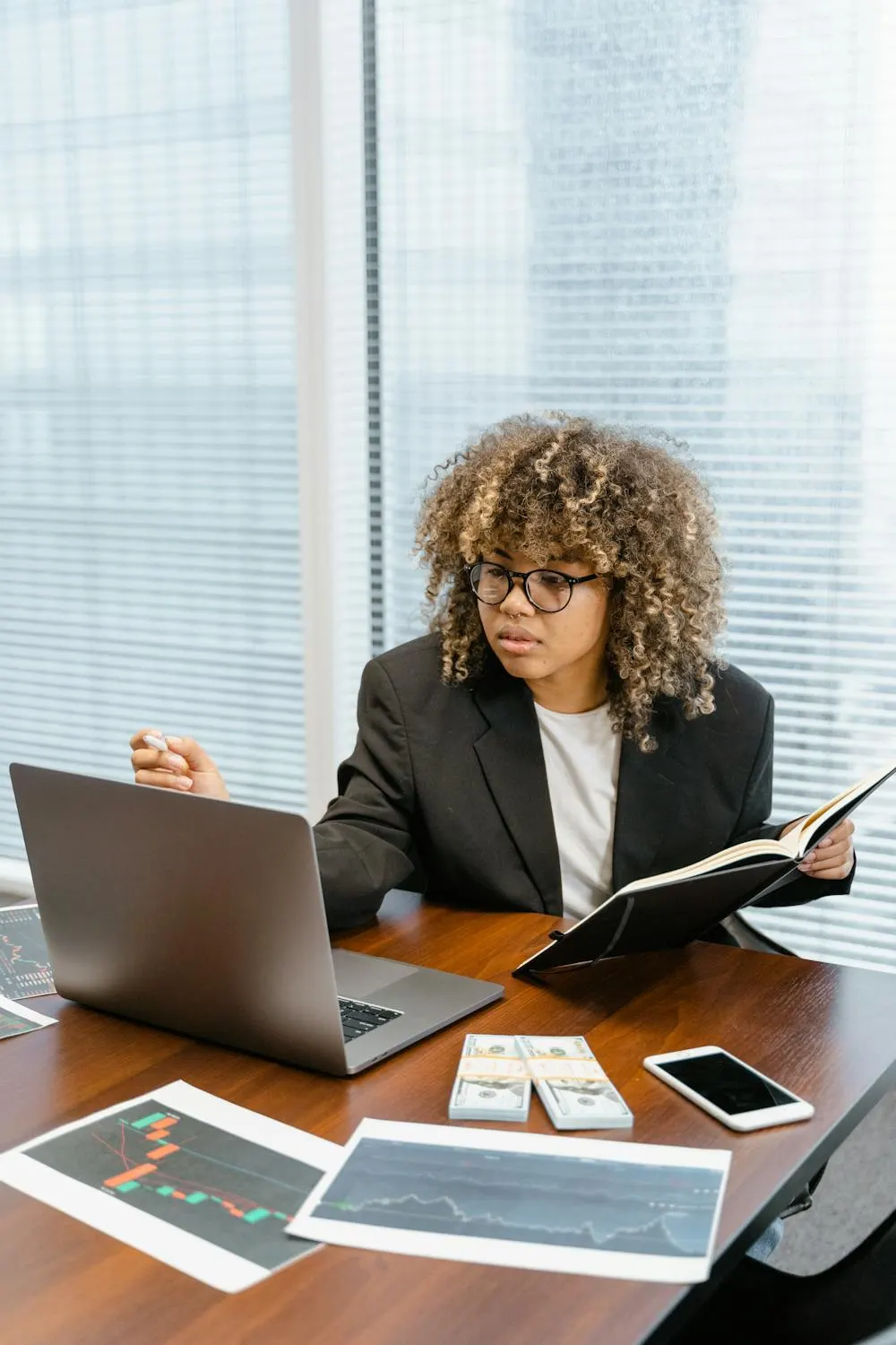 A trader reviewing a trading journal alongside printed charts and a laptop at a desk, planning before the session starts.
