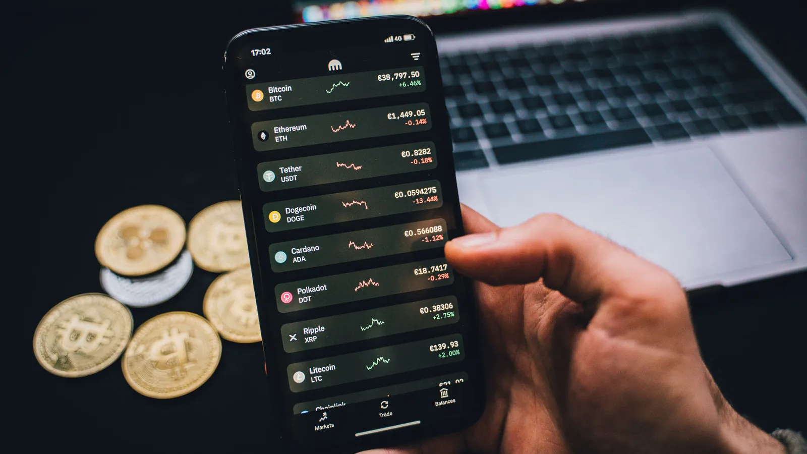 A trader checking crypto prices on a phone beside a laptop