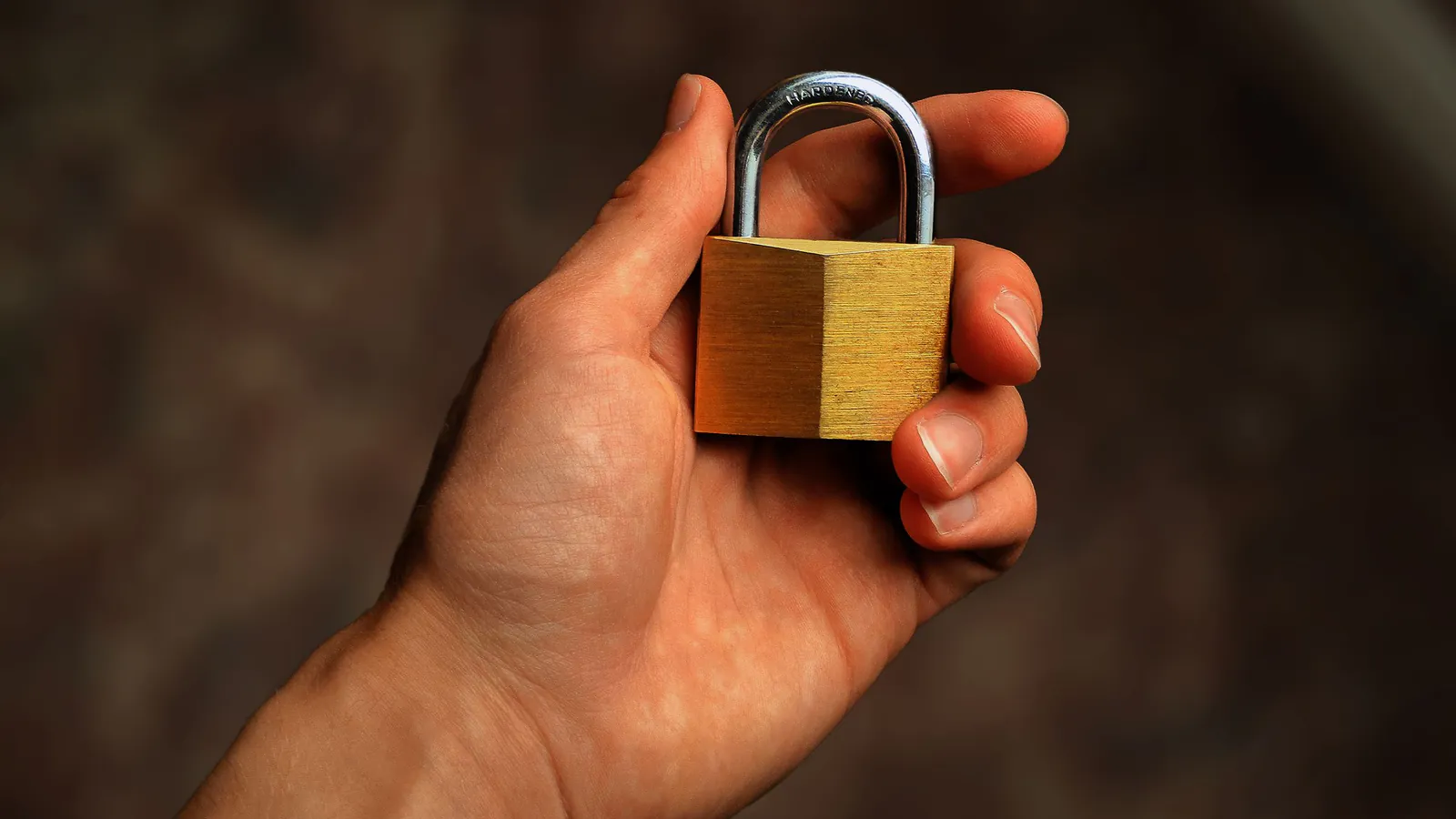 A hand holding a closed brass padlock