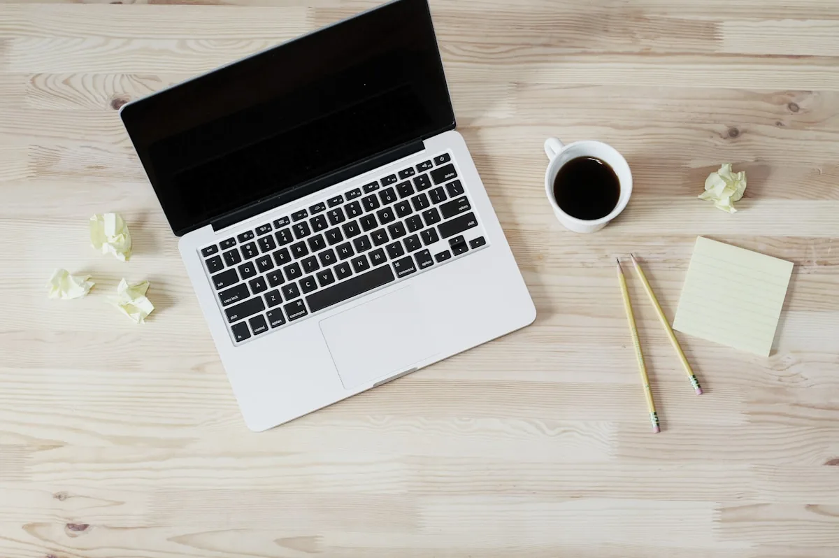 A laptop, notepad, pencils, and coffee on a desk, representing reviewing prop firm terms before committing