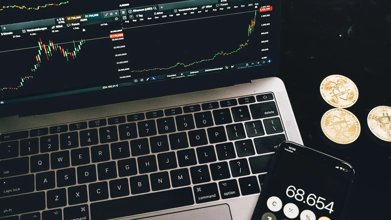 A laptop showing price charts beside a calculator and coins