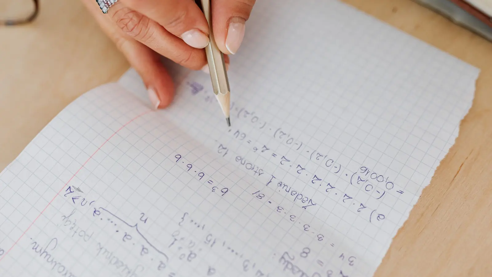 A hand working through a formula on squared paper