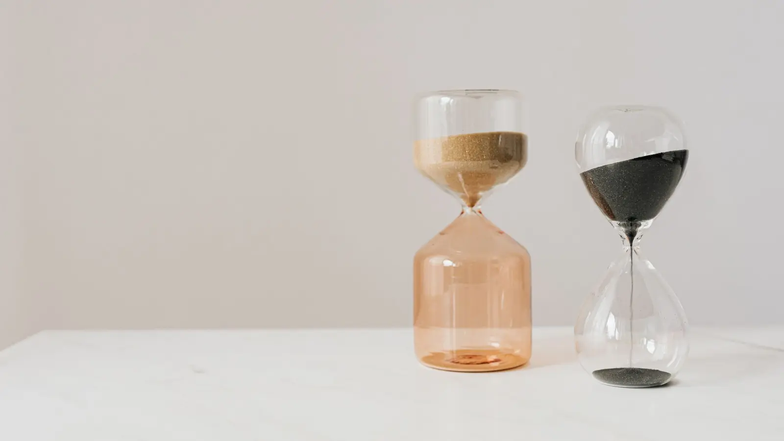 Two hourglasses with sand running on a white table