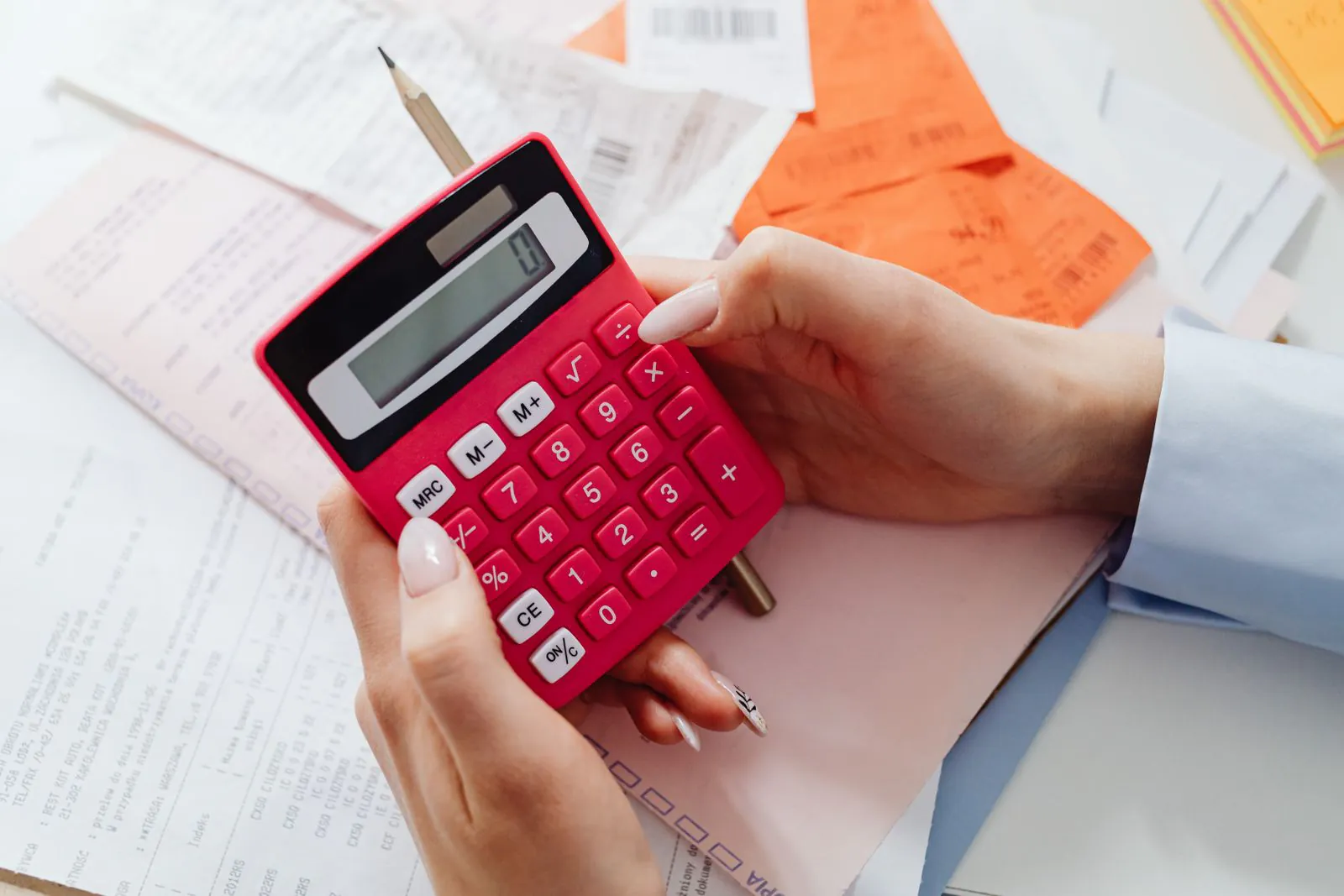 Hands working out costs on a calculator over a pile of receipts