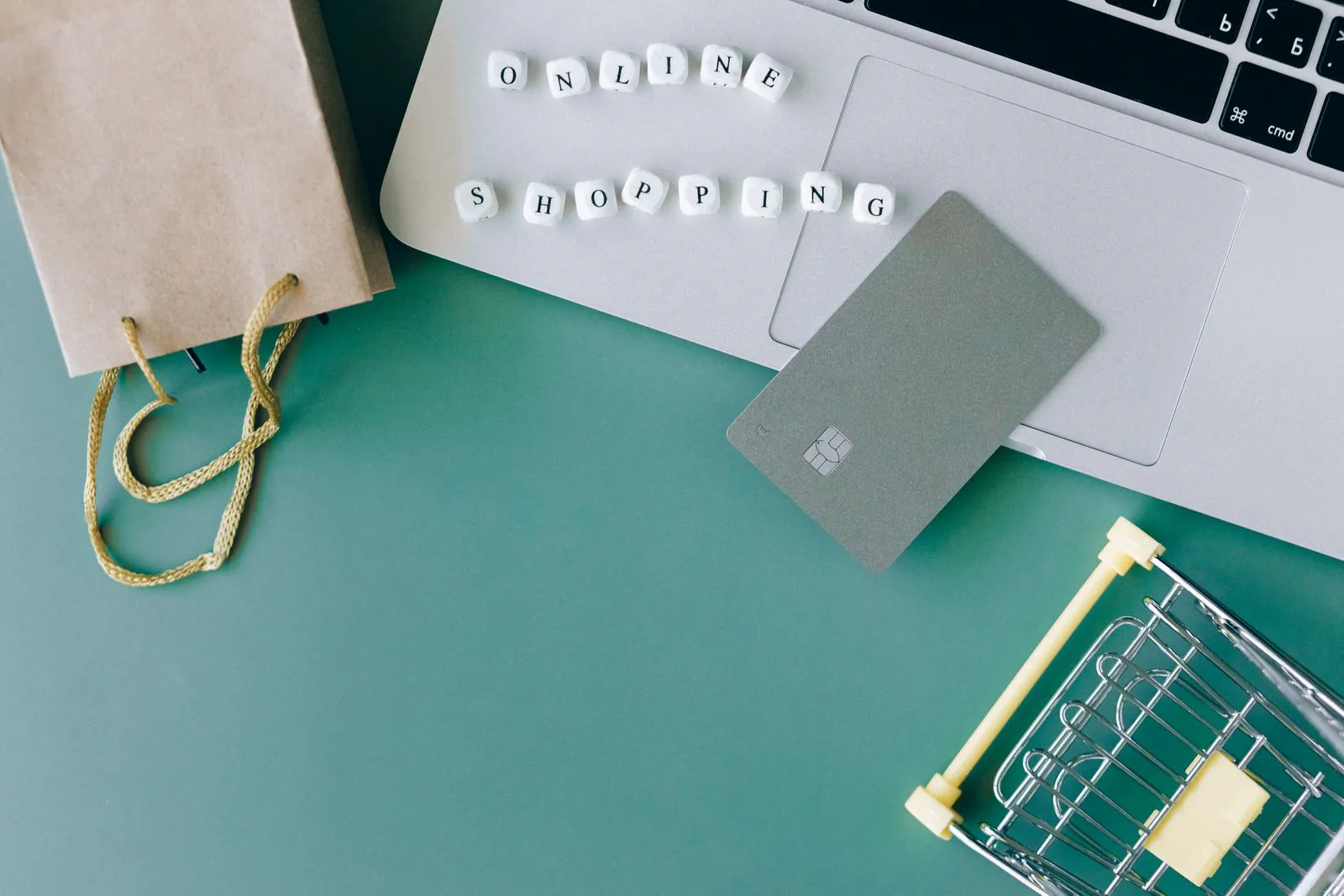 Bank card resting on a laptop next to a shopping bag and a small cart