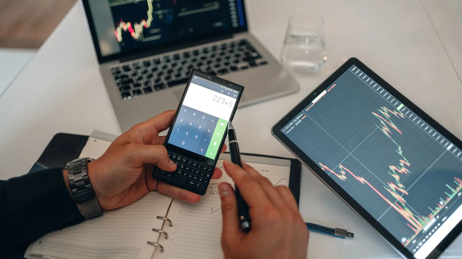A trader checking a chart on a phone next to a tablet and notebook