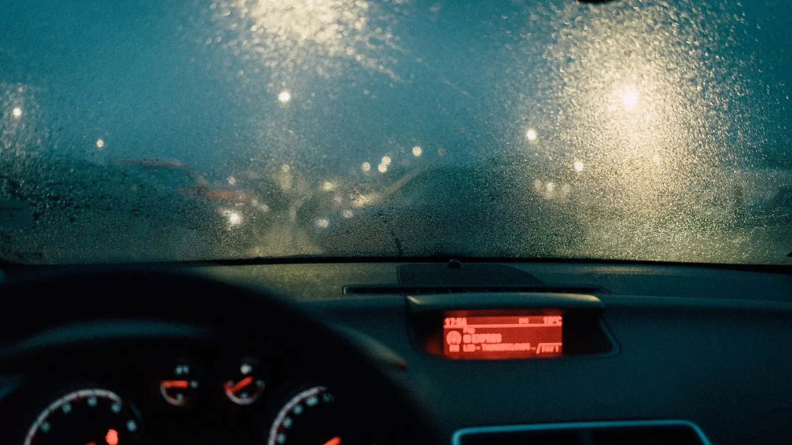 A rainy windshield at night with blurred traffic lights