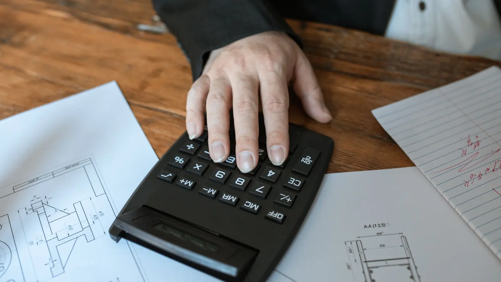 A hand on a calculator next to printed figures