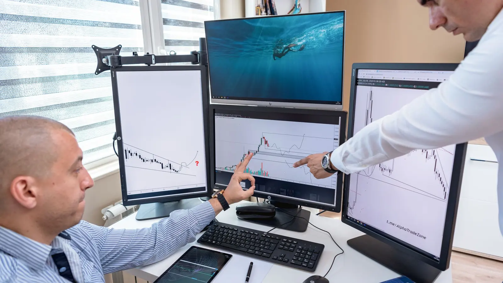 Two traders discussing charts at a multi-monitor desk