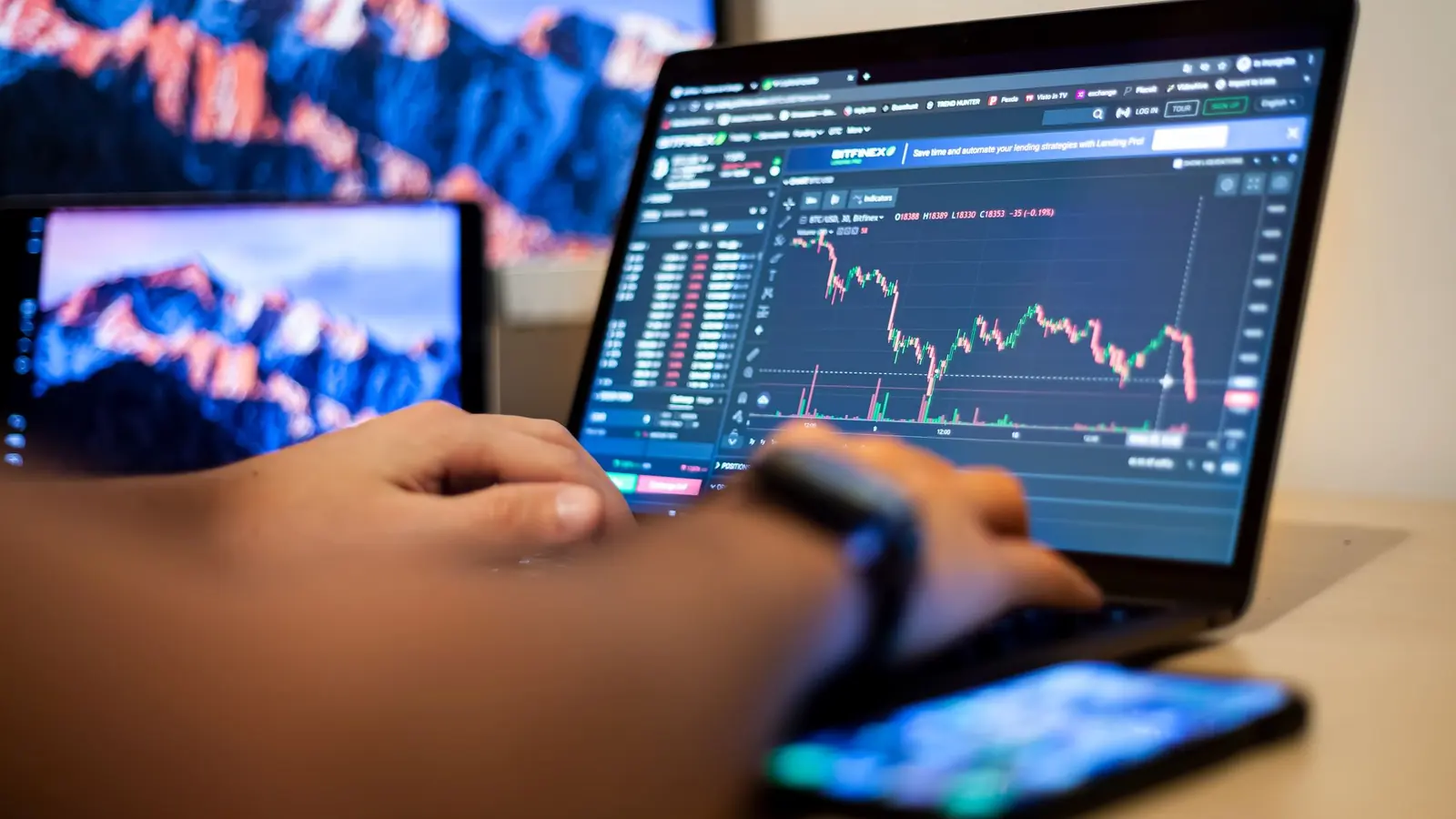 A trader checking a price chart on a laptop with a phone in hand
