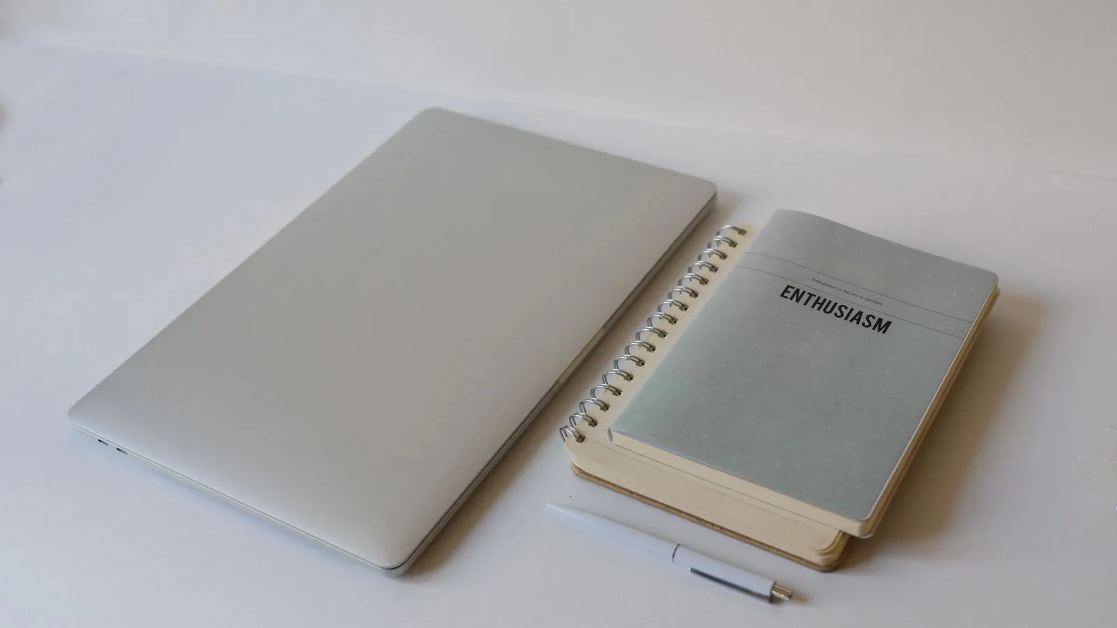 A closed laptop next to a notebook on a clean desk