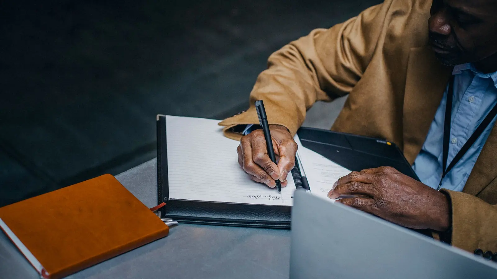 A trader writing notes in a notebook beside a laptop